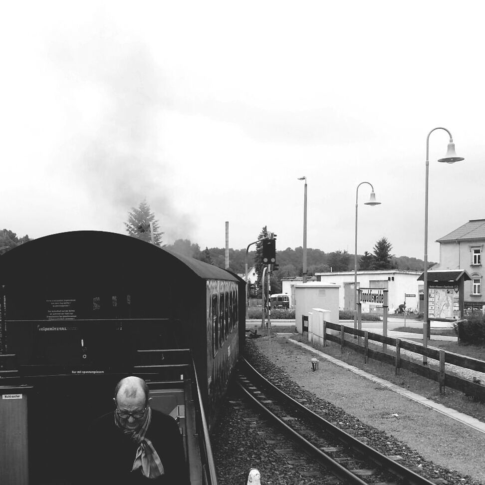 transportation, mode of transport, railroad track, sky, building exterior, land vehicle, rail transportation, car, built structure, architecture, public transportation, street light, train - vehicle, street, railroad station platform, railroad station, road, city, tree, day