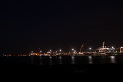 Illuminated port by sea against sky at night