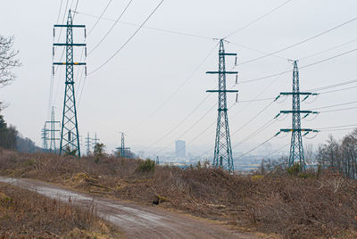 Electricity pylons on field against sky