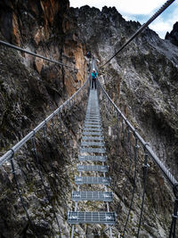 Woman standing on footbridge against rocky mountains