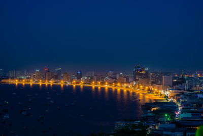 Illuminated city buildings against clear blue sky at night
