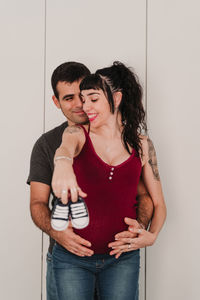 Pregnant couple holding shoes while standing against wall