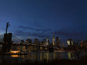 Illuminated buildings by river against sky at night