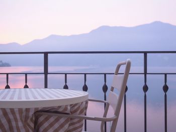 Chairs and table by swimming pool against sea during sunset
