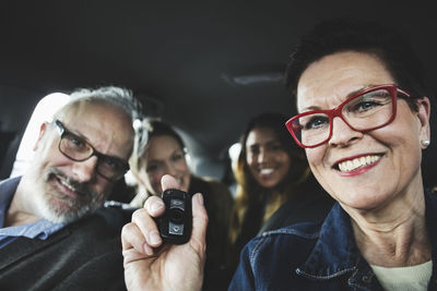 Smiling senior woman holding remote while sitting with people in car