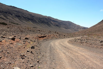 Dirt road by mountains against clear sky