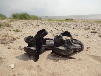 Close-up of shoes on sand at beach against sky