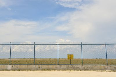 Fence on field against cloudy sky