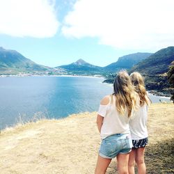 Rear view of women standing on field by river against sky