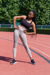 Athletic african woman does pelvic tilts to sides standing on red track of city stadium on sunny day