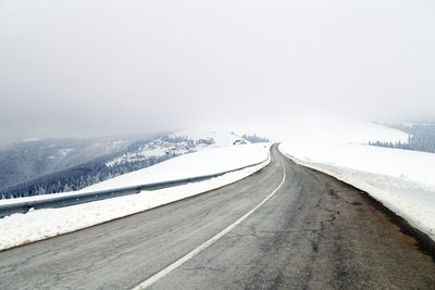 Road on snow covered landscape against clear sky