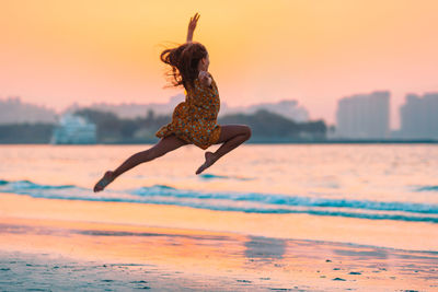 Woman jumping on beach against sky during sunset