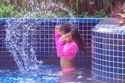 Side view of girl splashing water in swimming pool