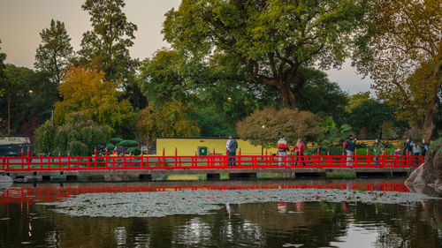People on footbridge over lake at park during sunset