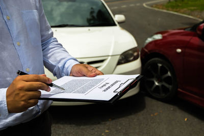 Midsection of agent reading insurance policy while standing on road