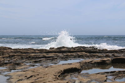 Scenic view of waves splashing on rocks against clear sky