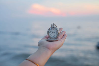 Cropped hand of person holding pocket watch at beach during sunset