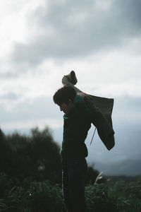 Man wearing jacket while standing in forest against sky