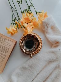 Old book, yellow flowers, black coffee and a fluffy blouse on a white table
