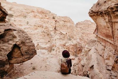 Rear view of young woman with backpack sitting on rock at desert against sky