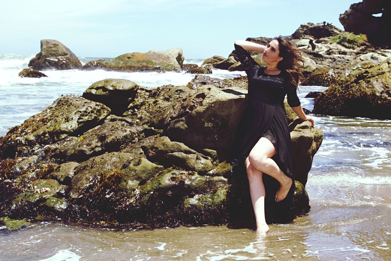 FULL LENGTH OF YOUNG WOMAN ON ROCK AT SEA