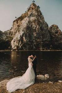 Couple standing on rock by lake against clear sky