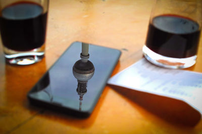 Reflection of fernsehturm on smart phone amidst drinks on table