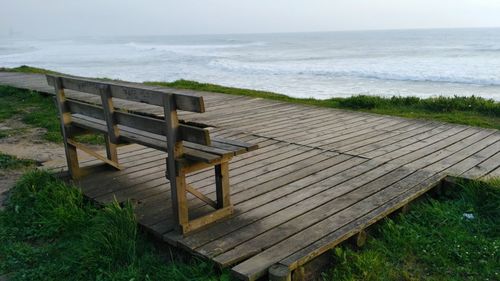 Empty bench on shore by sea against sky