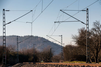Electricity pylon by railroad tracks against sky