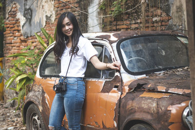 Portrait of smiling young woman standing by abandoned car