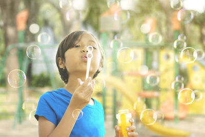 Girl blowing bubbles while standing in playground