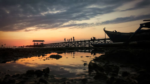 Silhouette bridge over sea against sky during sunset at untia beach, makassar city indonesia.