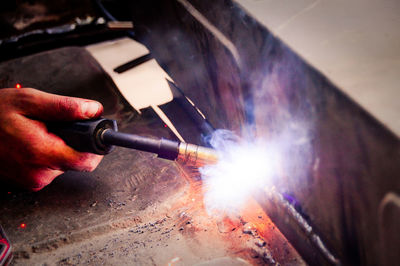 Cropped hand of welder welding metal in factory