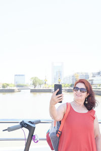 Portrait of woman wearing sunglasses while standing against river