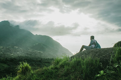 Man sitting on field against sky