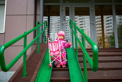 Toddler drags a toy stroller along the ramp of the stairs