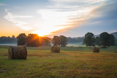 Hay bales on field against sky during sunset