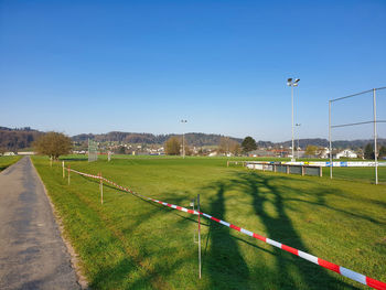 Street amidst field against clear blue sky