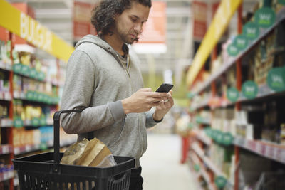 Man in supermarket comparing prices during inflation on cell phone