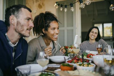 Smiling woman sitting with friends at dining table for dinner party