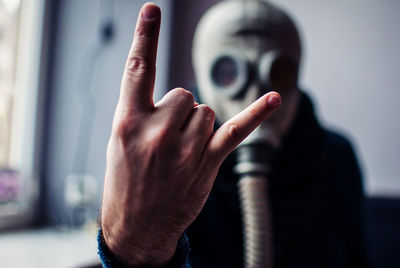 Close-up of man showing horn sign while wearing gas mask