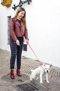 Happy young woman standing with dog on footpath