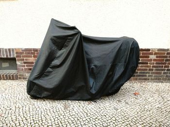 Motorcycle covered with black plastic against wall