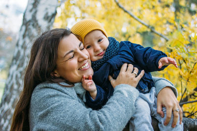 Smiling mother holding son against tree