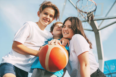 Low angle view of cheerful siblings playing with basketball against sky