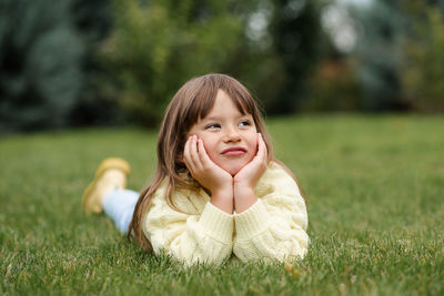 Funny smiling blonde little child girl 4-5 year old lying on green grass lawn outdoor. 