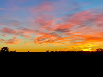 Scenic view of dramatic sky over silhouette landscape during sunset