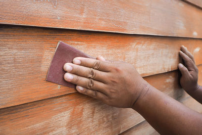 Cropped hands using sand paper on wooden wall