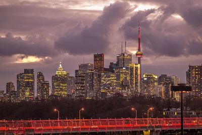 Illuminated buildings in city against cloudy sky