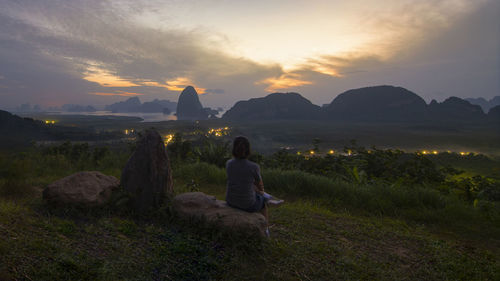 Rear view of woman sitting on land against sky during sunset